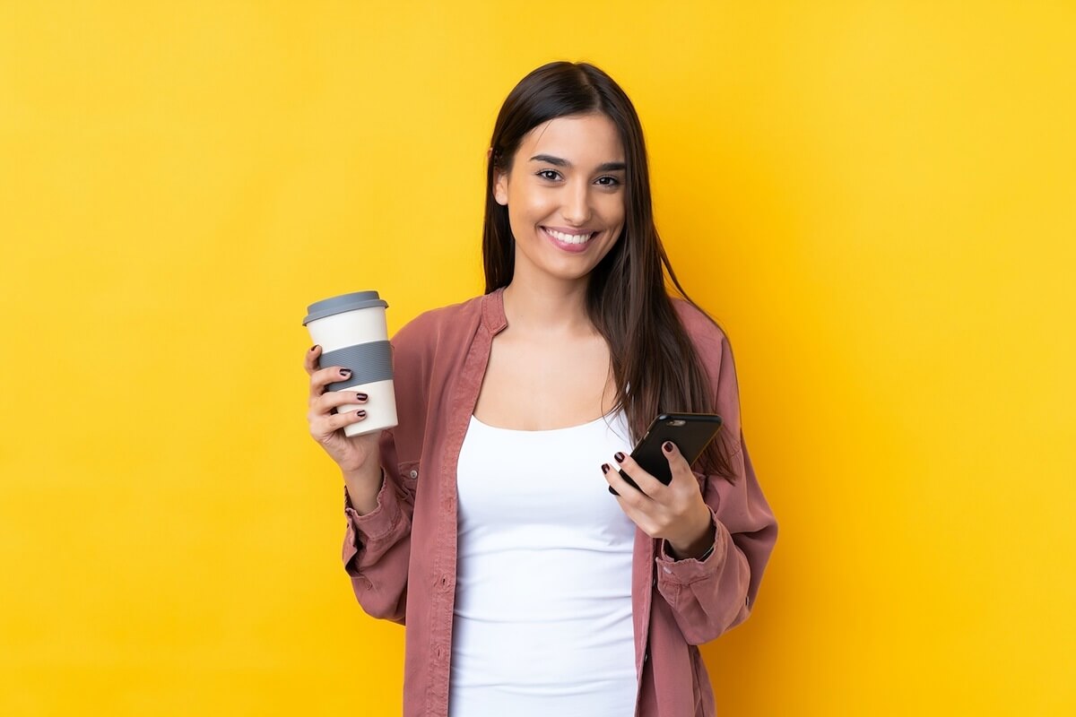 brunette girl using cell phone for EVV and holding coffee