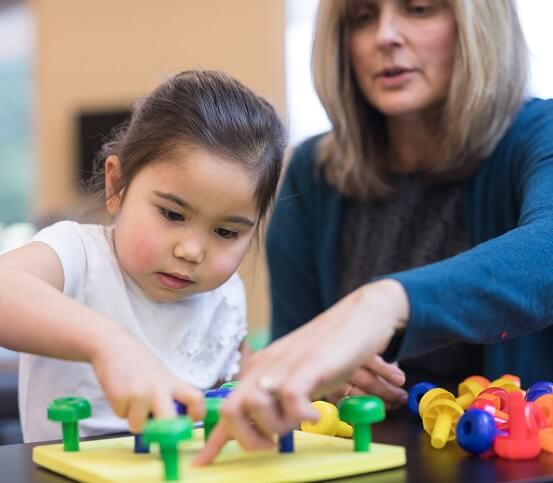 An occupational therapist works with a kindergarten-age ethnic girl on her coordination skills.