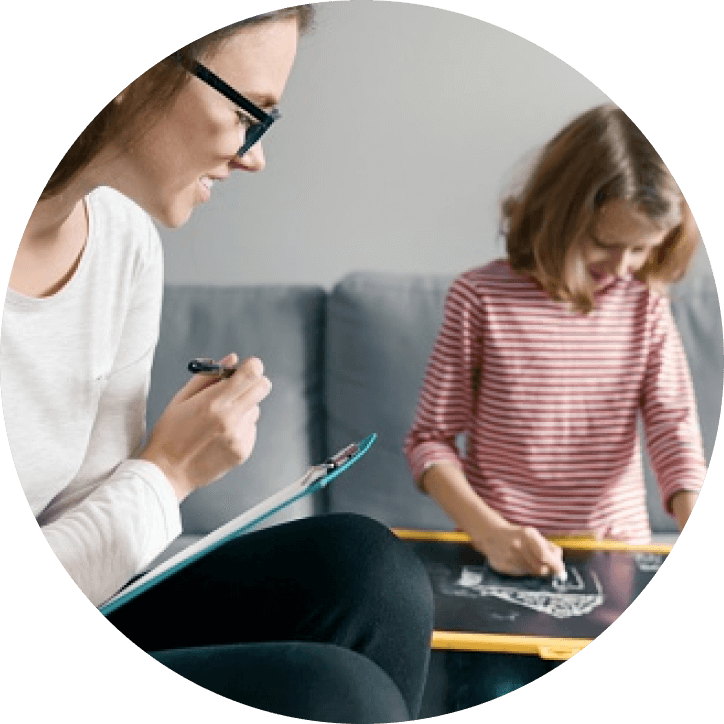 behavioral therapist looking at child draw on a small black board