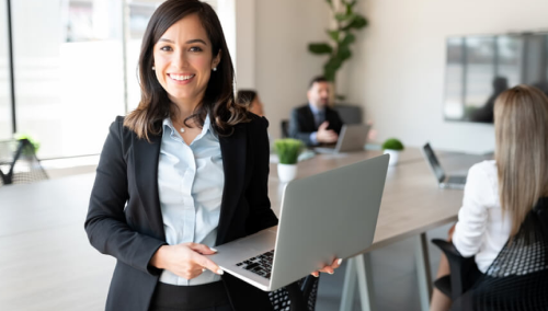 Woman smiling for a picture while holding laptop at work