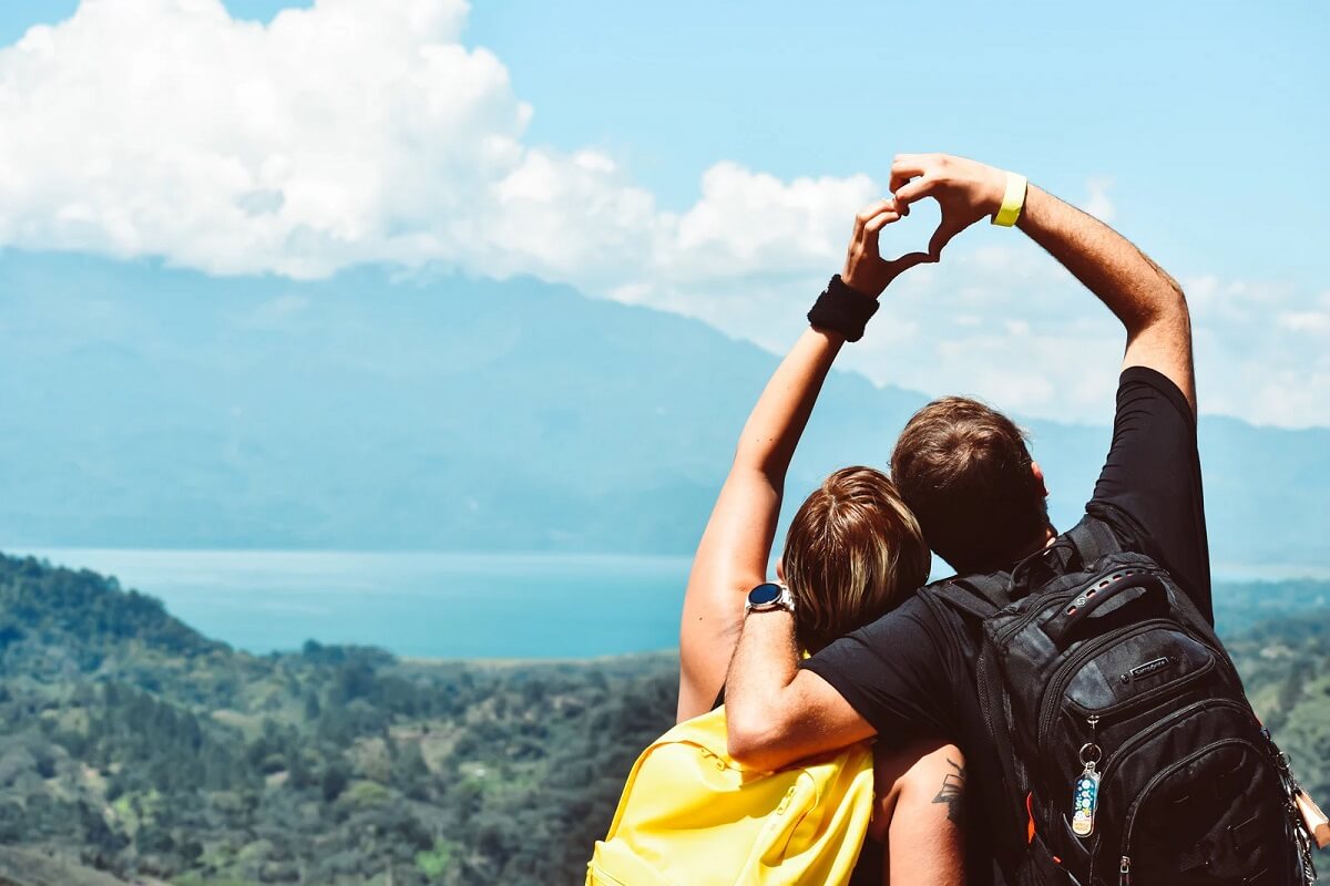 Couple hiking mountain on sunny day making heart shape with hands
