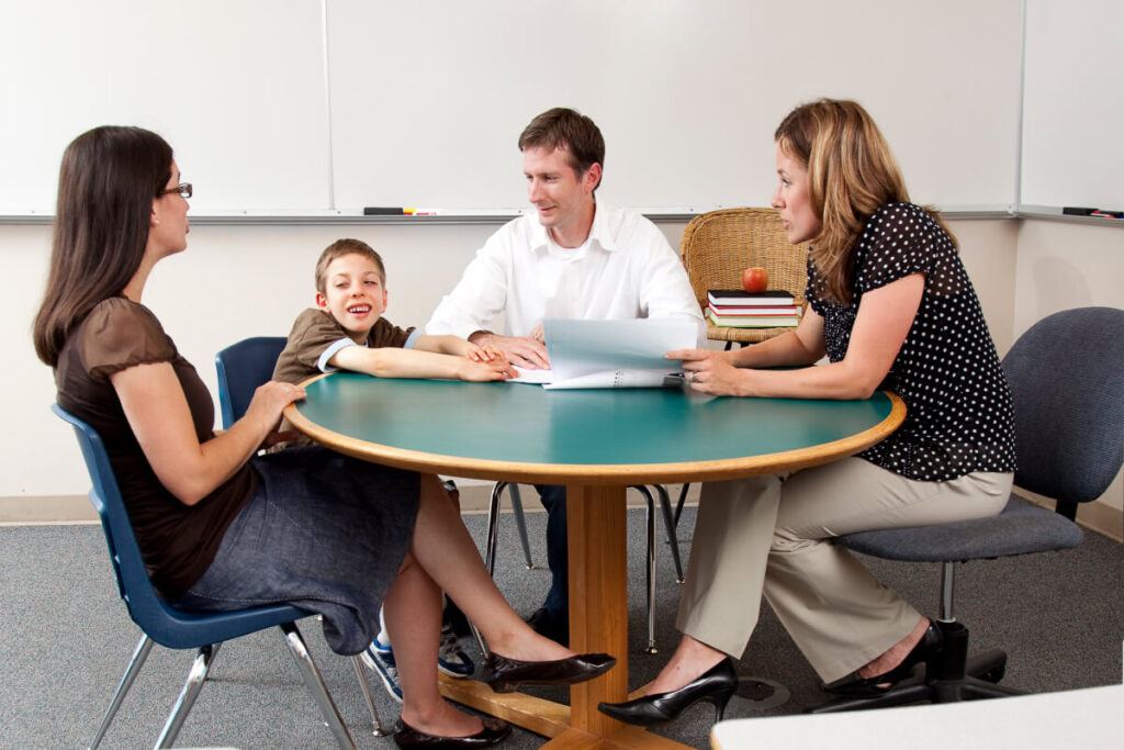 Two parents, their elementary aged son with disabilities, and ABA sitting in a classroom at a table