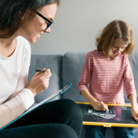 behavioral therapist looking at child draw on a small black board