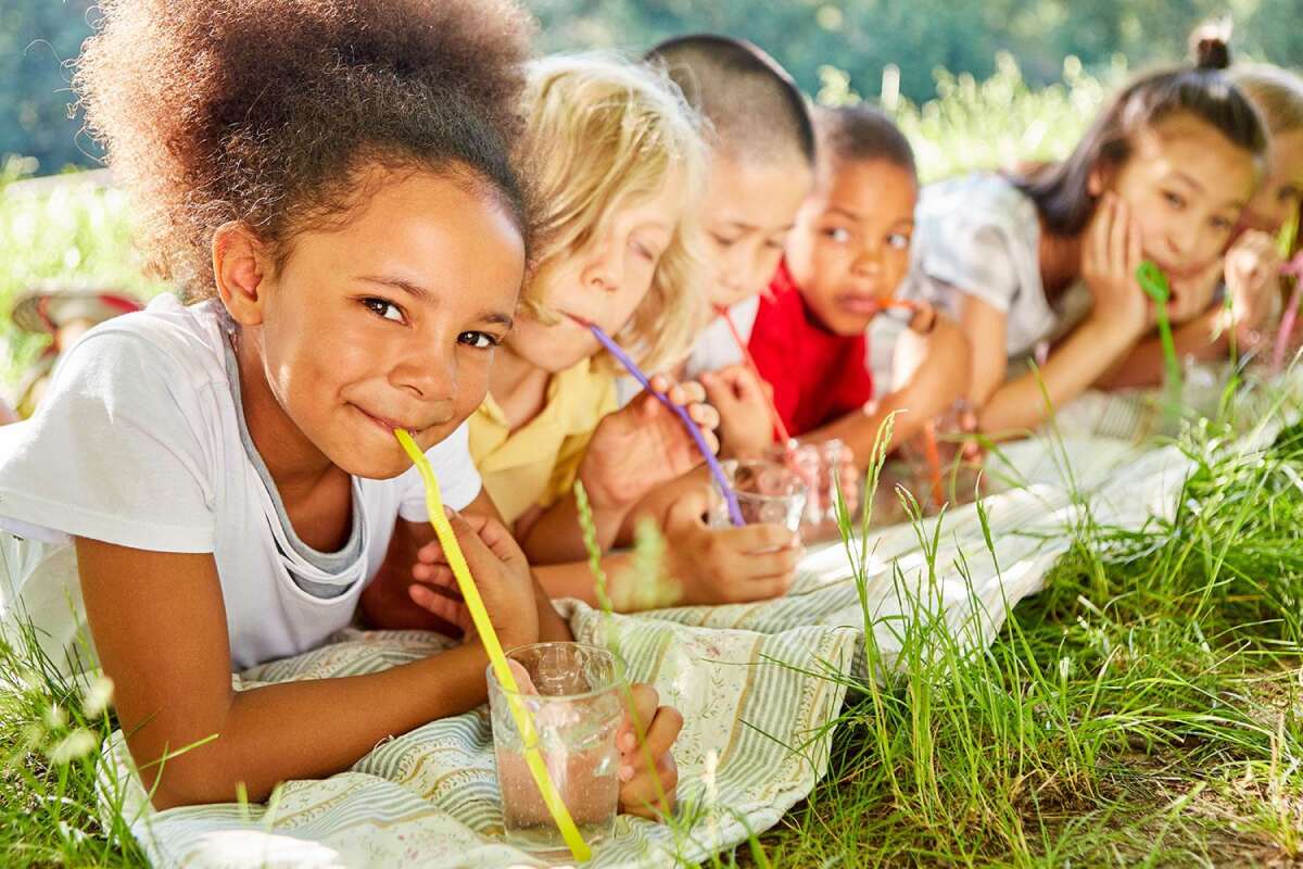 Children laying in field drinking from cups with colorful straws